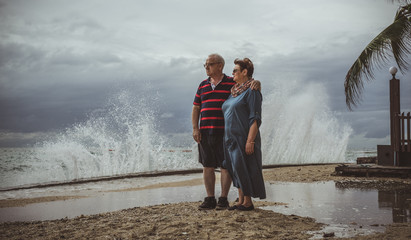 An elderly couple stands on the beach and watching as the approaching storm into the waves.