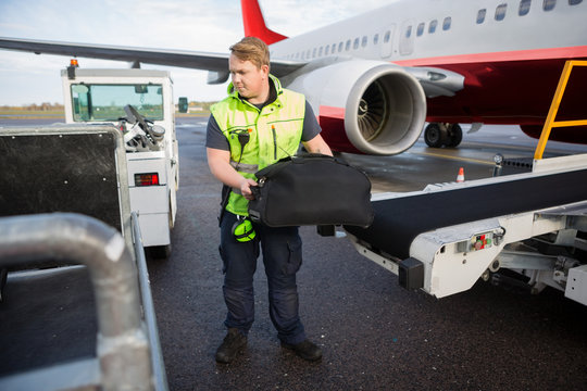 Worker Lifting Luggage From Conveyor Attached To Airplane