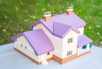 Layout of a house made of paper. Paper miniature beige cottage with a lilac roof against a background of green grass. Close up of handmade small house model. Architecture business concept