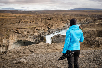 Fototapeta premium Female hiker looking at Aldeyjarfoss waterfall, Iceland. Female photographer holding a tripod.