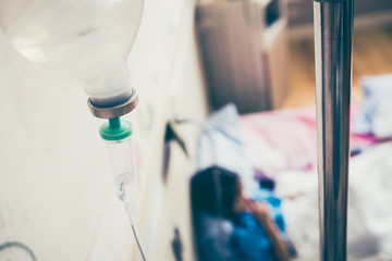 Illness asian girl sitting on sickbed in hospital with intravenous IV drip.