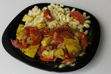 Pasta with stewed vegetables on a black dish isolated on a white background