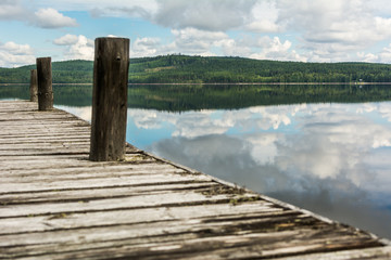 Old wooden pier on calm lake with reflection of mountains and cloudy sky. Dalarna region, Sweden