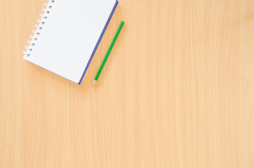 Note book and green pencil on beech color background with copy spech.