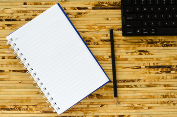 White note book and black pencil and black keyboard on bamboo color background with copy space.