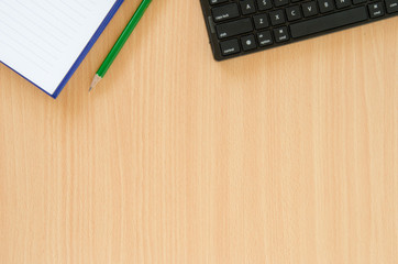 White note book and green pencil and black keyboard put on beech color table with copy space.