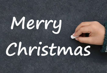 Fototapeta premium Little boy writing Merry Christmas on a blackboard