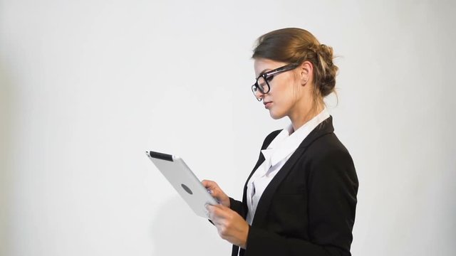 Good-looking young dark hair caucasian businesswoman, in a white blouse and a black jacket, is using her tablet in the white background, isolated, slow motion