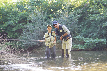 Naklejka premium Father teaching son how to fly-fish in river