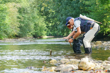 Father and son fly-fishing and catching rainbow trout in river