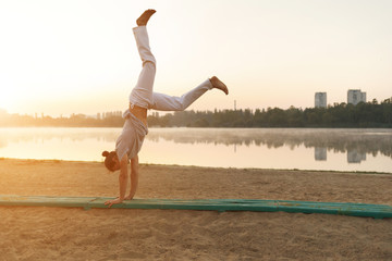 Fototapeta na wymiar Athletic capoeira performer workout training on the beach sunris