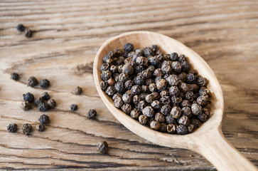 Black peppercorns in wooden spoon on rustic table