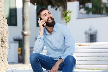 Handsome man sitting outside laughing and talking on mobile phone