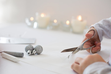 Close up photo of child´s hands holding scissors, cutting white paper, creating chrismas paper origami