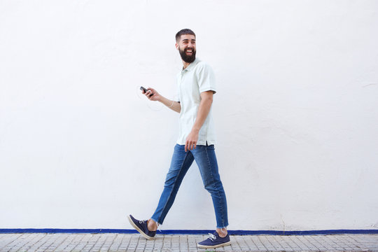 Full Length Man Walking And Holding Mobile Phone With Earphones