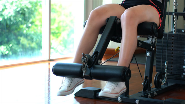 Legs Of Young Sport Girl Doing Seated Leg Curls On Machine In Gym