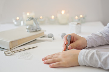 Photo of child hands holding a silver coloring pen, drawing a christmas present on a white paper