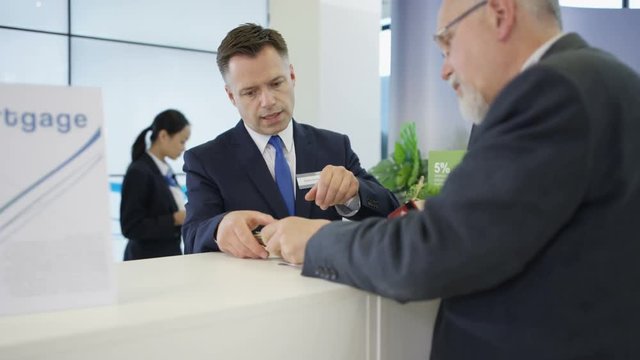  Bank worker at service desk taking cash deposit from a customer.