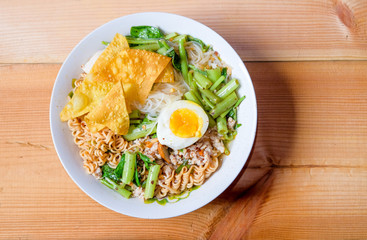 Tom yum noodles special put a small line, instant noodles, convolvulus, boiled egg and dumpling in a bowl of white paste on wood chamcha, on top view and use of natural light for photography.