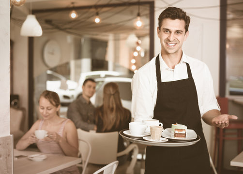 Waiter holding served tray meeting visitors at pastry bar