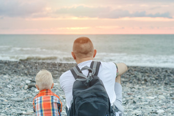 Young father and son are sitting on the beach of sea