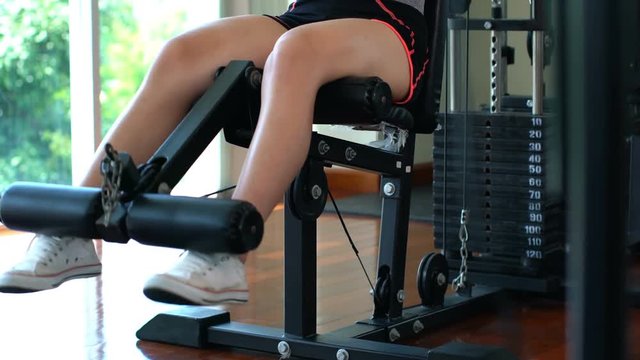 Legs of young sport girl doing seated leg curls on machine in gym