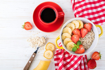 Breakfast with oatmeal porridge, coffee cup, berries and fruits. Oatmeal with strawberries and banana. Healthy breakfast concept. Top view