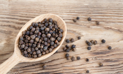Aromatic black peppercorns in wooden spoon. Food and spicy concept