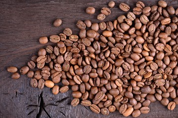 Naklejka premium Coffee beans on an old wooden desk. Top view of coffee beans with a copy space for your text. Natural coffee background.