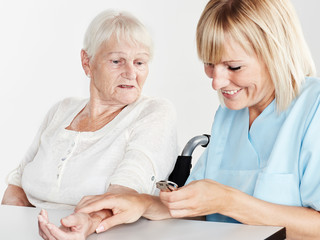 Pflegerin kontolliert Puls von Seniorin