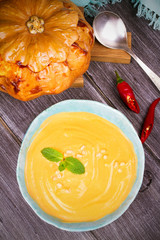 Creamy pumpkin (or butternut squash) soup in a bowl, whole roasted pumpkin on wooden background. View from above, top studio shot, vertical