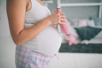 Home portrait of young pregnant woman preparing for childbirth and doing everyday homework at nursery
