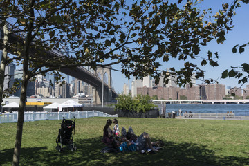 view of NYC from beneath the Brooklyn Bridge in a park with picnicers