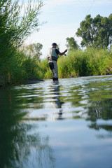 Fly fisherman catching trout in river