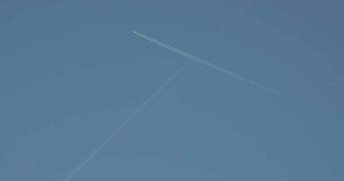 A distant airplane passes high overhead, leaving a jet contrail against a clear blue sky.