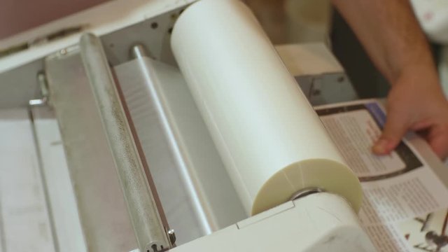 Hands of caucasian man run a roll laminator during its work