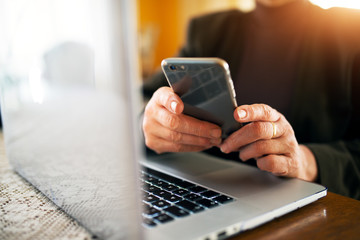 Close up of a senior businesswoman looking at mobile while working from home with a laptop.