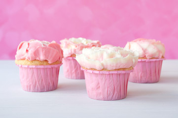 Pink cupcakes with white whipped cream in form of flower on white wooden table and pink background. Picture for a menu or a confectionery catalog.