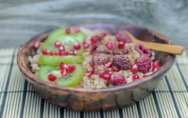 Healthy diet wellness cereal flakes homemade breakfast: Glass or ceramic Bowl of oatmeal wheat rye porridge, hot healthy food with fruits and berries: kiwi, peeled pomegranate seeds, raspberries