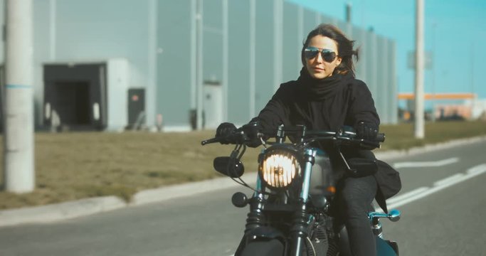 TRACKING Beautiful Caucasian female biker riding her motorcycle near warehouse. 4K UHD RAW edited footage