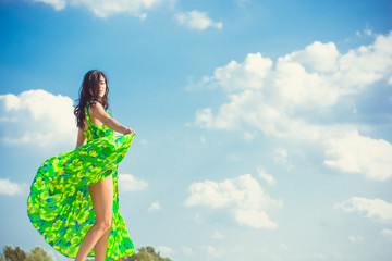 Pretty young woman in a bright green long dress on a background of nature demonstrates spectacular clothes and herself