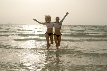 Two pretty playful girls running in the sea hugging each other.