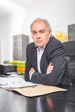 &Auml;lterer Mann mit wei&szlig;em Hemd  sitzt auf einem Stuhl und bl&auml;ttert in einer auf Dokumenten Akte