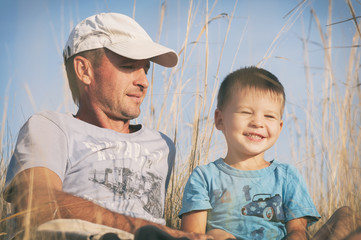 father and son are sitting in the field, father hugs his son, toned photo