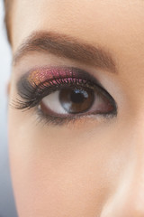 Opened brown eye of a young pretty girl with perfect, healthy skin color and beatiful evening make-up made by eyeshadows, glitter and mascara. She has high perfectly formed eyebrow and long lashes.