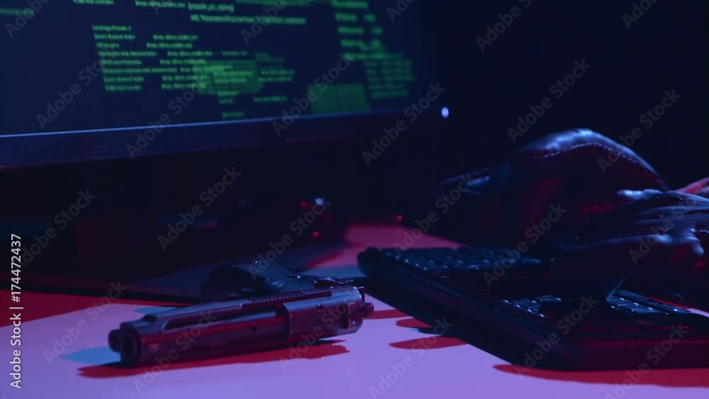 Poster hacker types the virus data, on the table there is a pistol. close up
