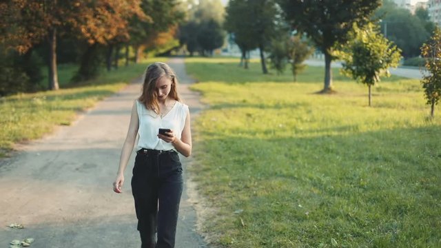 Full view young attractive woman holding smartphone walking green park footpath summer mobile sightseeing internet concept 3g browsing trendy lifestyle cellphone media social business lady device