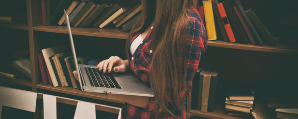 Young woman holds a laptop and book shelves on background