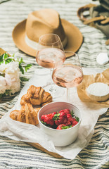 French style romantic summer picnic setting. Flat-lay of glasses of rose wine with ice, strawberries in bowl, croissants, brie cheese, straw hat, peony flowers, square crop. Outdoor gathering concept