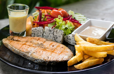 Salmon grill steak with french fried and vegetable salad on black plate